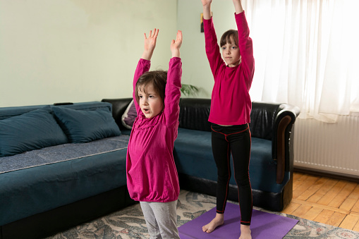 Two small girls whit hand raised exercise on a mat in living room