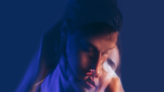 Inner duality. Neon portrait. Double exposure of pensive thoughtful woman with head down isolated on dark blue background.