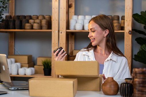 Caucasian young woman packing vase goods order into box for customer. Beautiful attractive business girl work to preparing parcel boxes checking ecommerce shipping online retail to sell at home store.
