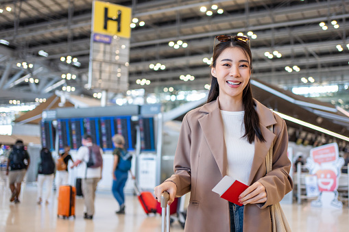 Portrait of Asian young girl walk in airport terminal to boarding gate. Attractive beautiful female tourist passenger feel happy and excited to go travel abroad by airplane for holiday vacation trip.