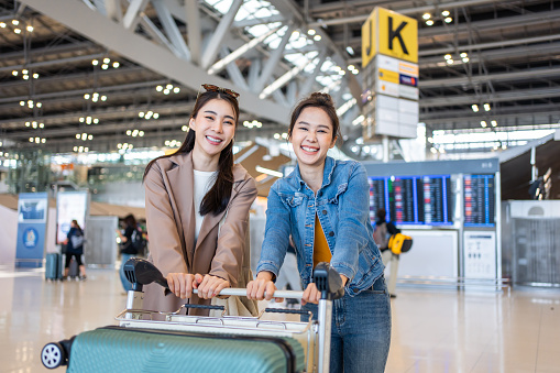 Portrait of Asian women standing in airport terminal at boarding gate. Attractive beautiful female tourist passenger feeling happy and excited to go travel abroad by airplane for holiday vacation trip