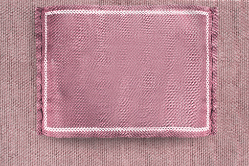 Blank pink clothes label stitched on pink fabric background closeup