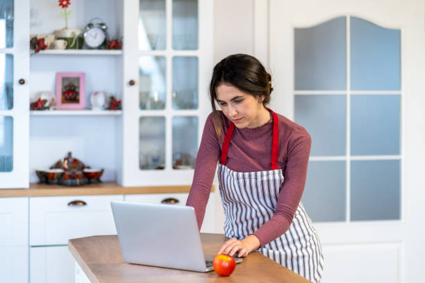 istock Young female baker sitting on kitchen counter typing on laptop 1693422966