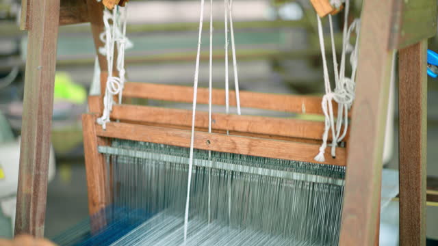 Unrecognized senior woman using wooden traditional loom for weaving fabric from various colored yarns in the northern of Thailand, close up shot of the working of antique loom for making the cotton fabric