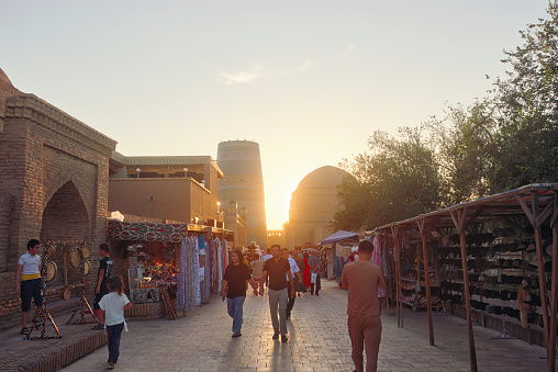 Khiva, Uzbekistan - July 8 2023: Numerous tourists from different countries walk at sunset in the historical part of Ichan-Kala, the walled inner city of Khiva, Uzbekistan. UNESCO World Heritage Site.