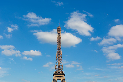 The Eiffel Tower, a wrought-iron lattice tower on the Champ de Mars in Paris, France photographed through trees during a summer day.