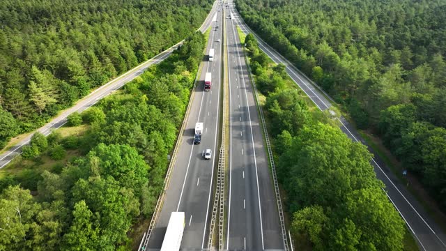 Aerial footage of traffic on the four-lane freeway in the midst of a forest, following a car with a bike and camper trailer. A shot of vacationing on wheels.