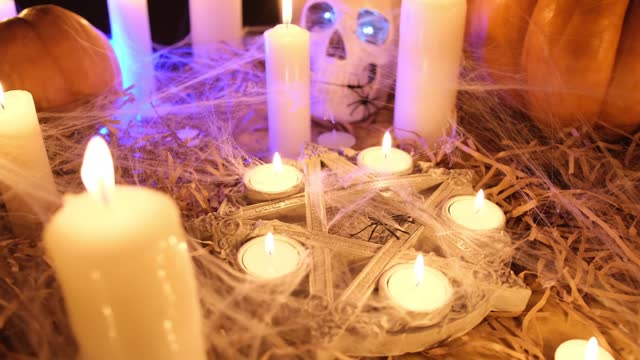 Traditional pumpkins with old skull and burning candles in cobweb among dry grass and spiders