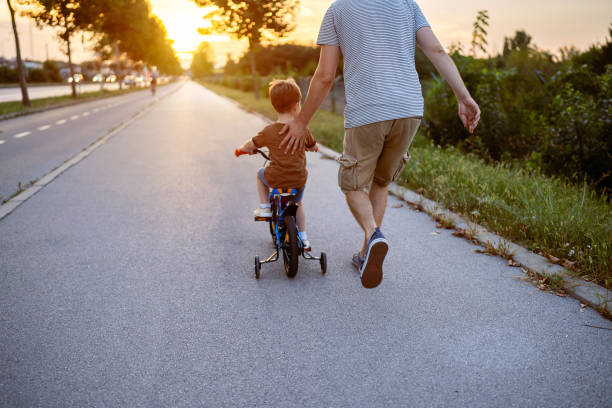 père enseignant de son fils à faire de la bicyclette - roue stabilisatrice photos et images de collection