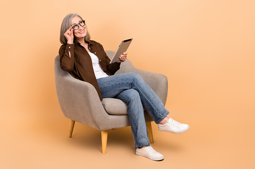Full body length photo of dreaming middle age woman look thoughtful mockup trading broker hold tablet isolated on beige color background.