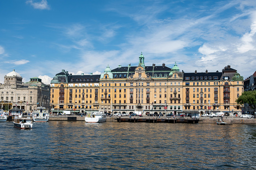 Stockholm, Sweden. Waterfront imposing building at Strandvagen embankment in Ostermalm district. Moored boat at port, blue sky background.