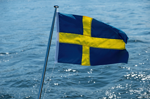 Sweden national flag waving on boat flagpole, blur sea water background, sunny day,
