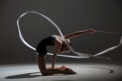 Rhytmic gymnastics female routine with ribbon. On knees leaning backwards and interesting ribbon shape.