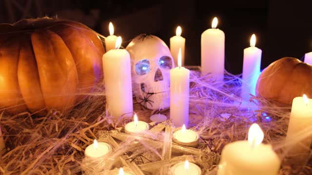 Halloween orange pumpkins, candles, human skull, pentagram in cobweb among dry grass in dark spirits night