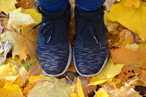 woman feet in black running trainers on the ground with dry yellow leaves