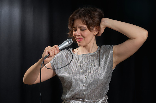 Portrait of a singing woman with a microphone in her hands on a black background