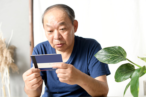 An elderly Asian man is surprised to see his bank account passbook.