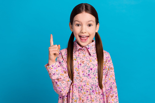 Photo portrait of pretty schoolkid point up empty space idea dressed stylish pink flower print outfit isolated on blue color background.