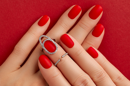 Close up womans hands with matt nails on red background. Manicure, pedicure design trends. Beauty salon concept