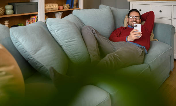 istock High angle view of smiling businessman text messaging over smart phone while lying on sofa at home 1693478134