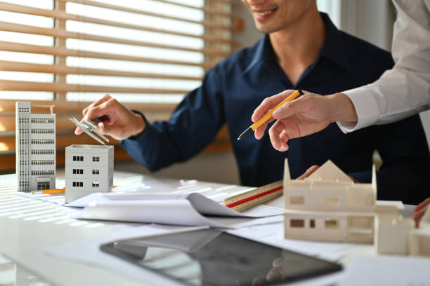 istock Two architects man examining house model and reviewing blueprints in a creative office 1693493251