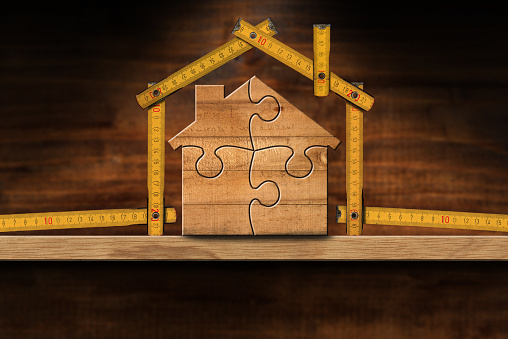 Wooden house made from a folding ruler and jigsaw  puzzle pieces, on a wooden workbench with copy space. Construction industry and interior design concept.