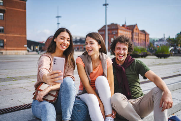 istock Three happy tourists taking selfies while sitting on steps in the city square 1693495234