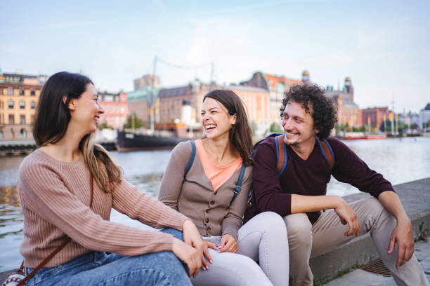 istock Three happy tourists sitting by the river and talking 1693496015