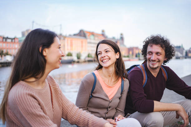 istock Three happy tourists sitting by the river and talking 1693496021