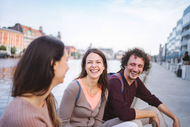 istock Three happy tourists sitting by the river and talking 1693496557