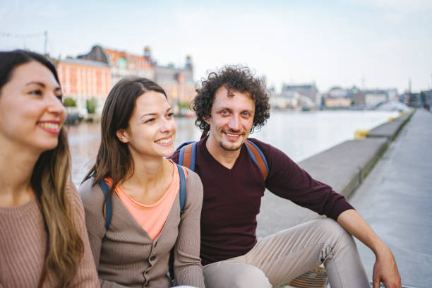 istock Three happy tourists sitting by the river and talking 1693496612