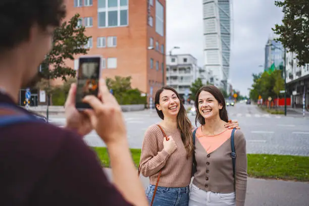 Two female bestfriends having their photo taken by their male friend in the city