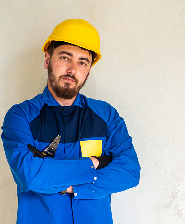 Portrait of worker or engineer in blue work clothes and yellow safety helmet with space for text. A man at a construction site holds an Insulation stripper in his hands and looks at the camera.