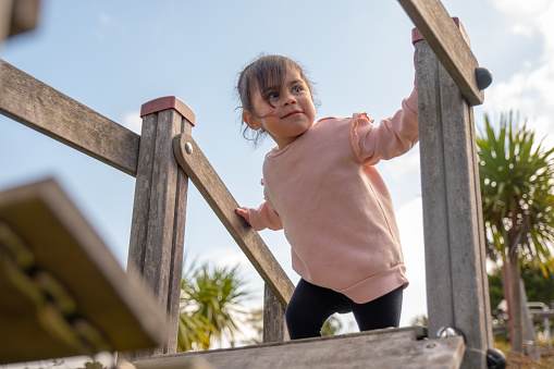 Baby girl holding on to handrails while climbing up playground