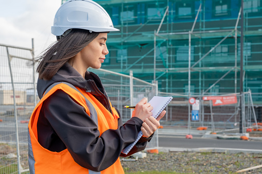 A female wearing construction clothing writing on a notepad