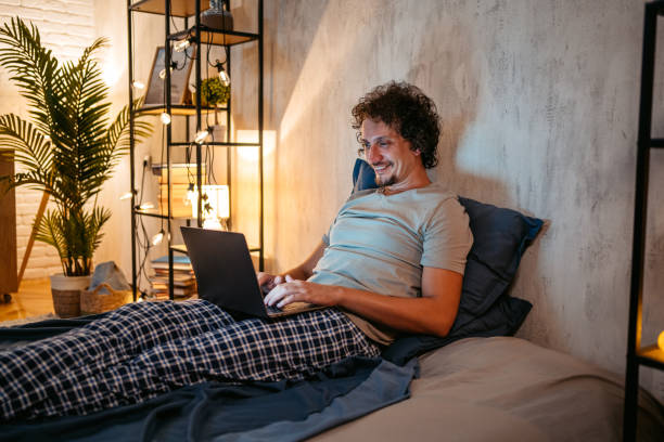 istock Young Man Working On The Laptop From His Bed At Night 1693529006