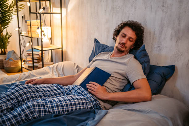 istock Young Man Falling Asleep While Reading A Book In The Bed At Night 1693533018