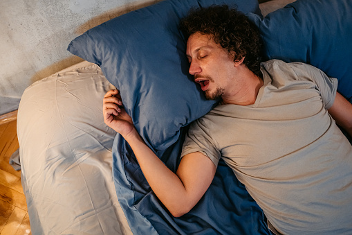 Handsome young man sleeping in the bed at night in his bedroom. Snoring and having breathing problems.