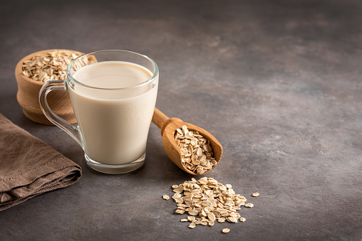 Oat milk in a glass on a brown rustic background. Side view, selective focus. Copy space.