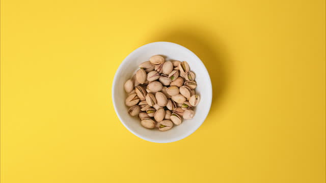 Pistachios in a bowl on a bright yellow background. Stop motion video with the pistachios nuts disappear from the bowl