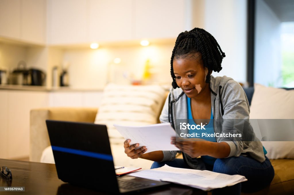 Female student with vitiligo skin reading notes studying at home Young woman studying at home working on laptop in living room 25-29 Years Stock Photo