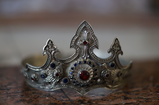 A shiny silver crown rests atop a dark wooden table, surrounded by a thin metal band