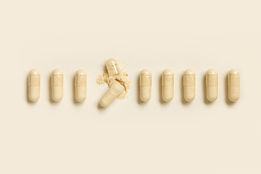 Medical capsules in a line with one opened to show beige powder on light beige top view. Preventive medicine and healthcare, dietary supplements and vitamins