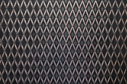 Fragment of the flooring made of black corrugated metal sheet. The pattern has the shape of a grid of diamonds. Close-up. Background.
