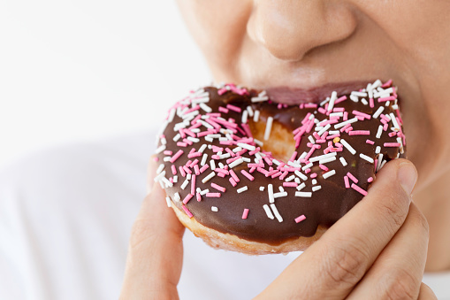 Caucasian woman is eating doughnut with sprinkles in front of white background