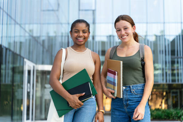 istock Two University Student girls looking at camera smiling outdoors at business college campus 1693586342