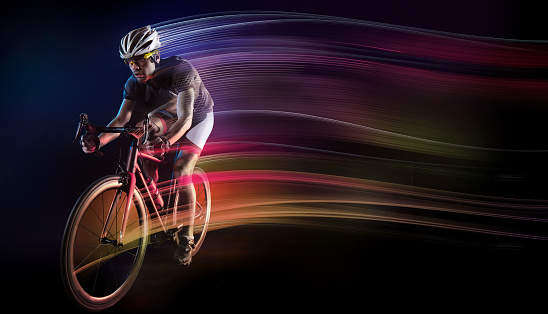 Professional male cyclist riding a racing bike on the open road at sunset. With international motion blur and lens flare.