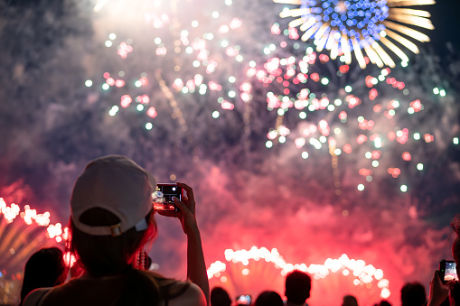 The back of a girl in a baseball cap filming a fireworks display on her mobile phone