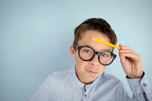 cool, cute young schoolboy with blue shirt, black glasses and pencil in front of blue background
