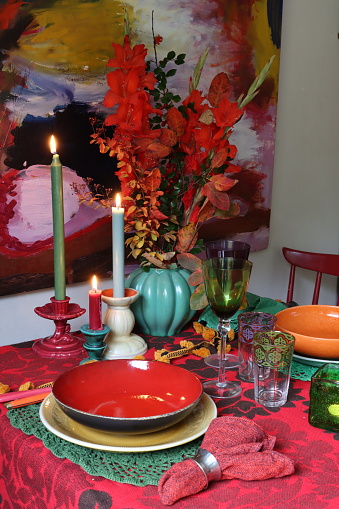 A Captivating Autumn Tablescape with Vibrant Porcelain, Glowing Candlelight, Red Tablecloth, a Leafy Bouquet in a Vase, and a Background Oil Painting. Crafted by a Talented Artist.